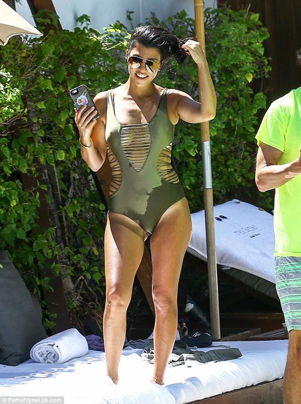 Kourtney Kardashian stretches at the poolside, giving an extra view of her tanned shoulder. 