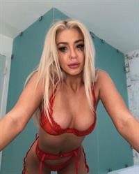 Tana Mongeau in sexy red lingerie showing off her big boobs cleavage in a bra and thong panties.