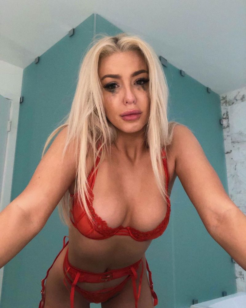 Tana Mongeau in sexy red lingerie showing off her big boobs cleavage in a bra and thong panties.